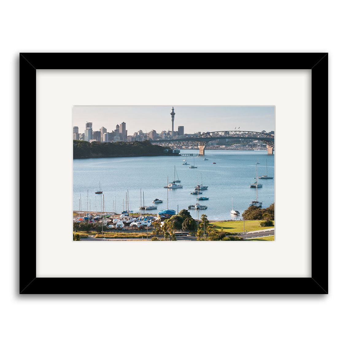 Framed photographic print Little Shoal Bay - RP229 features a New Zealand cityscape with sailboats, a bridge, and skyline with tall tower. Matted in archival quality matte paper and finished in a sleek black frame.