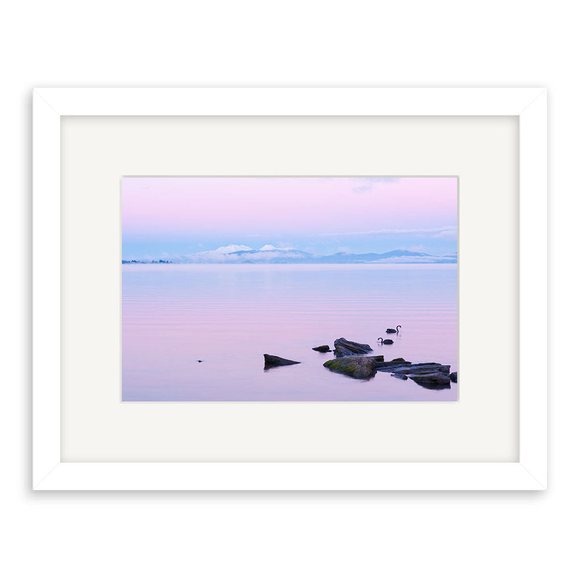 The Lake Taupo - RP237 is a framed photographic print featuring a tranquil New Zealand lake with scattered rocks, two birds by the water, and distant mountains beneath a pastel pink and blue sky on archival matte paper.