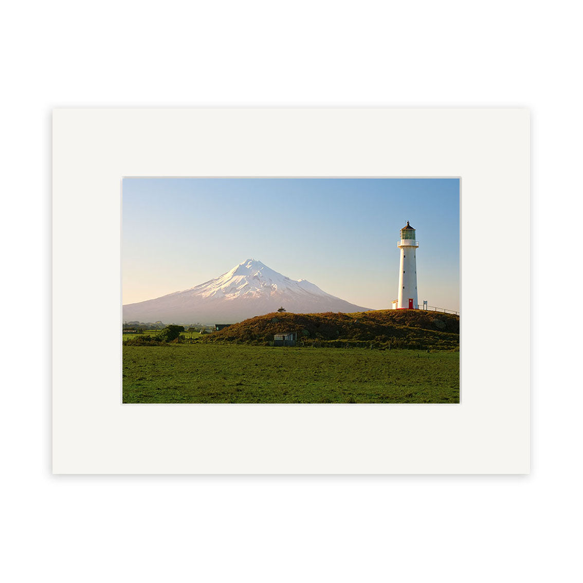 Cape Egmont - RP240 showcases a lighthouse on a grassy hill with a snow-capped mountain behind, beneath a clear blue sky, printed on archival quality matte paper for premium photographic display.
