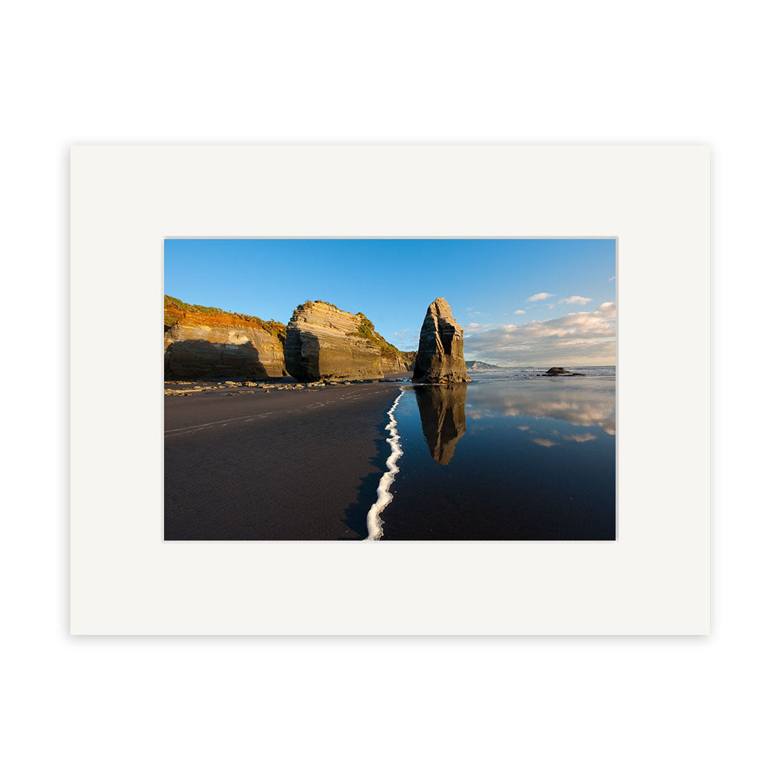 A photograph titled Tongaporutu - RP242 features New Zealand beach rock formations, with white sea foam leading towards them, under a clear sky reflected in wet sand—ideal for photographic prints on archival quality matte paper.