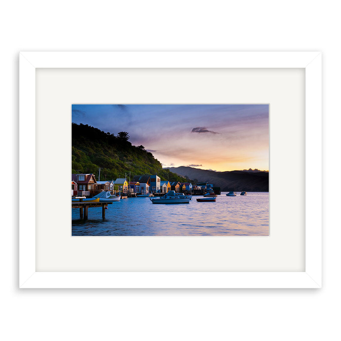 Paremata - RP248: Framed photographic print of a New Zealand waterfront at sunset with colorful houses, anchored boats, and tree-covered hills—printed on archival quality paper for lasting beauty.