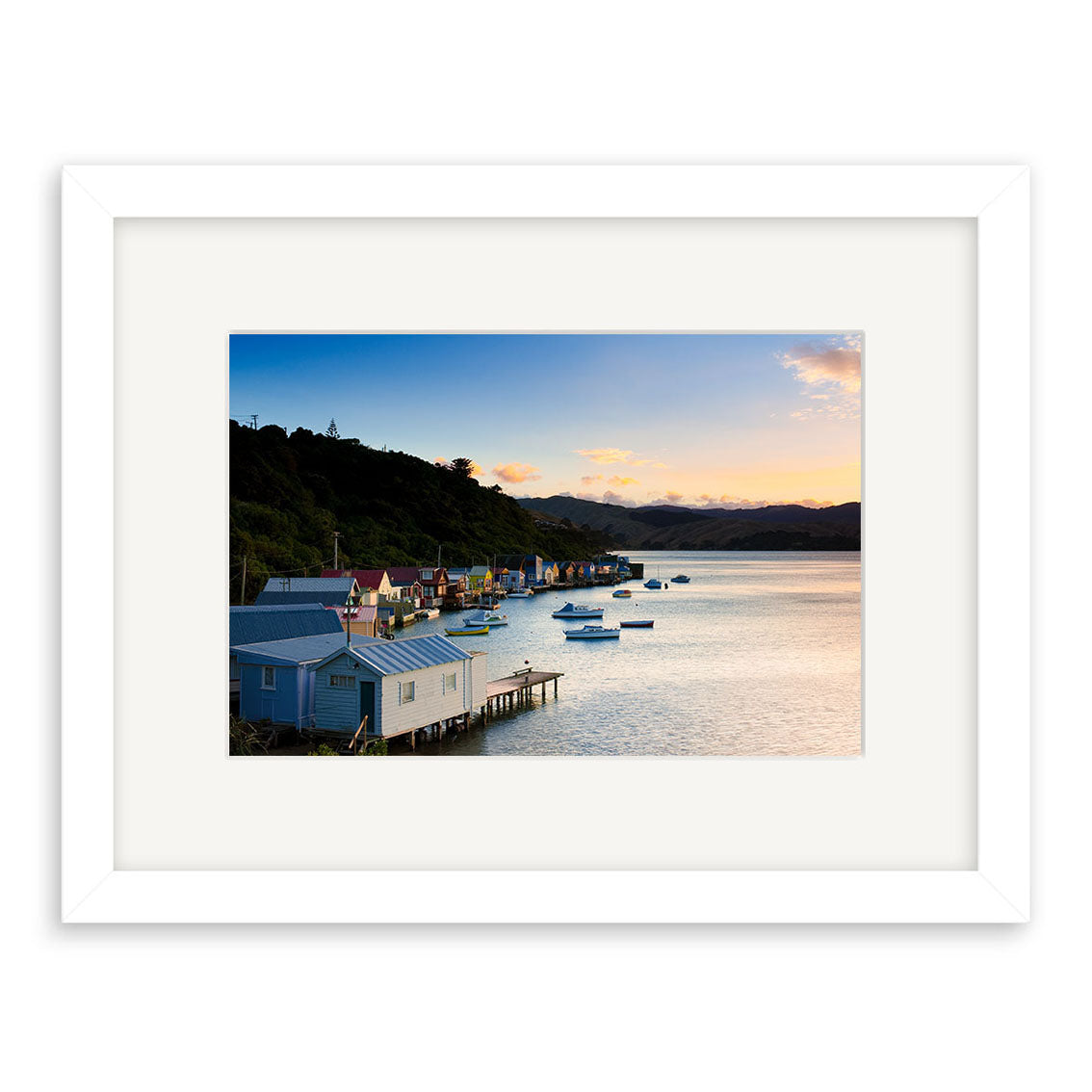 Paremata View - RP249 by Reuben Price: a framed photo capturing colorful boathouses, boats, and hills at sunset. Enjoy serene New Zealand photography with archival quality prints.