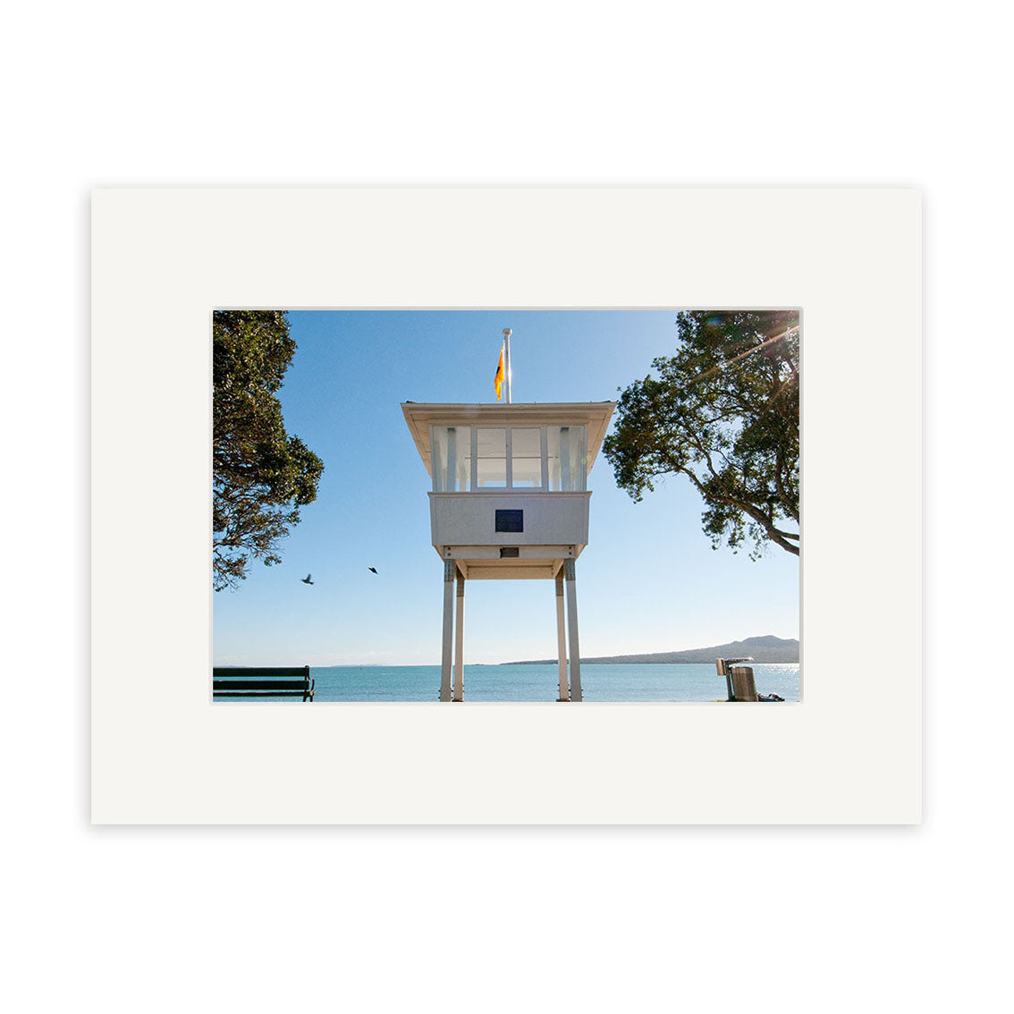 Narrow Neck 2 - RP251 features a white lifeguard tower on stilts by the water, among trees under a clear blue sky with two birds. A bench is partly visible. Available as photographic prints on archival quality matte paper.