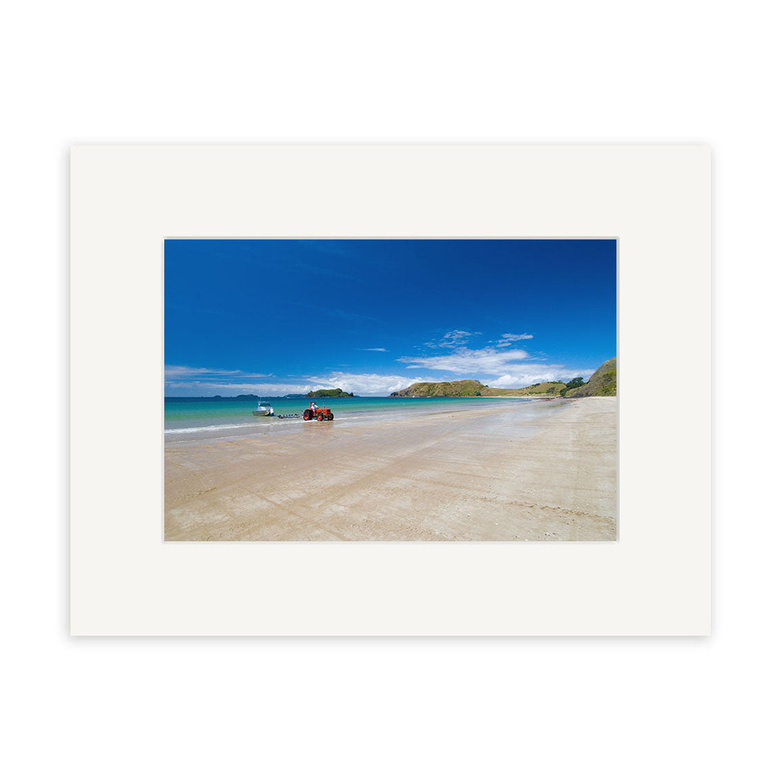 Opito Bay - RP254 features a wide sandy New Zealand beach with two small boats by the shore, calm blue sea, and green hills under a clear sky. Presented with a white mat on archival quality matte paper.