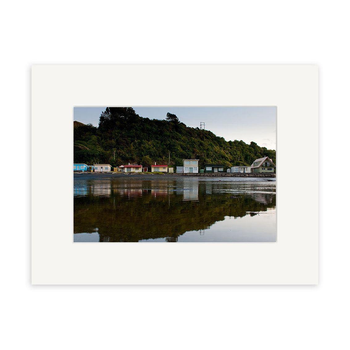 Tongaporutu Baches - RP258 captures small houses along the shore before a forested hill, their reflections in calm water—a classic New Zealand scene ideal for archival quality matte photographic prints.