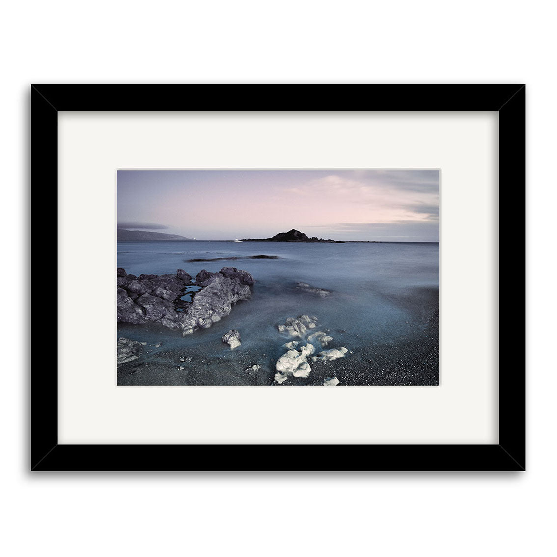 “Island Bay - RP260” is an archival-quality photographic print showing a calm New Zealand seascape at dusk with gentle waves, rocky foreground, and a distant island beneath a pastel sky.