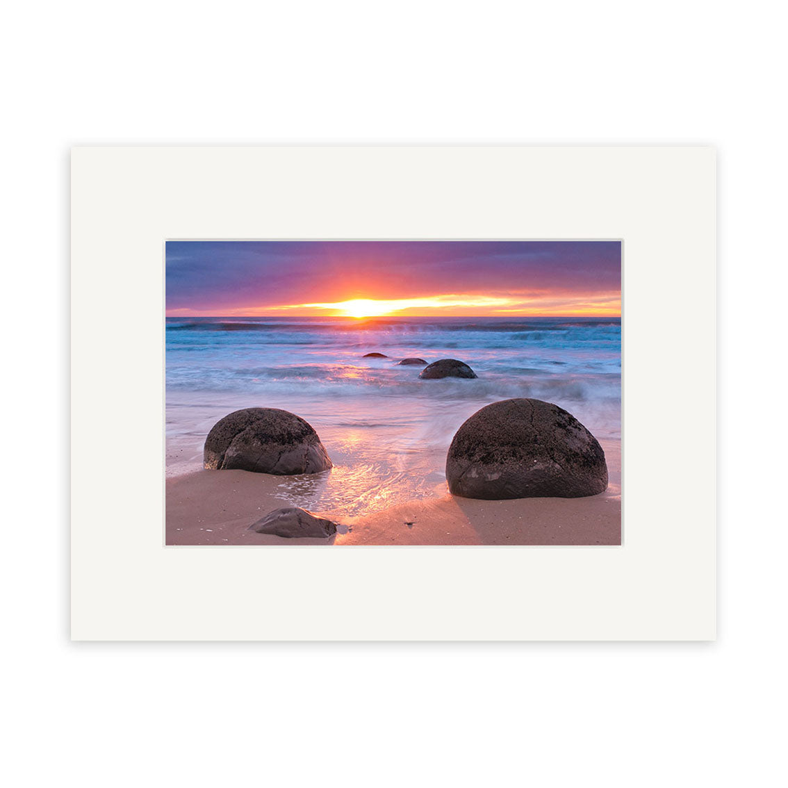 Moeraki Boulders - RP262: A vivid sunset over a New Zealand beach, waves lapping at the sand and large round boulders beneath an orange, pink, and purple sky—ideal for archival quality photographic prints.