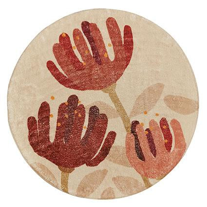 The Raw Pohutukawa Rug is a super-soft round beige floor rug with three red and orange stylized flowers, stems, leaves, and an anti-slip backing for safety.