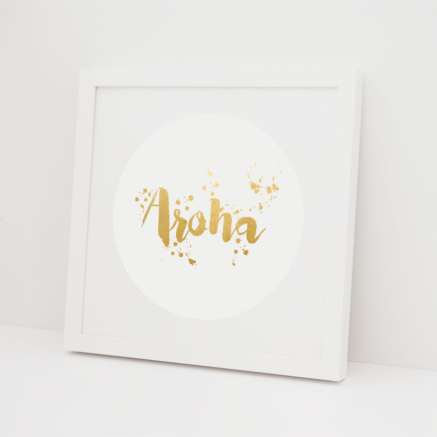 The Aroha Foil Print features Aroha in gold, brushstroke-style lettering with gold splatter accents, centered on a white background in a white frame—ideal for lovers of gold foil prints.