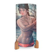 The Nymph Table Lamp is a cylindrical lamp with wooden feet, featuring J.H. Lynch’s print of a woman in red swim bottoms standing in water, set against a softly painted mid-century backdrop of trees and water.