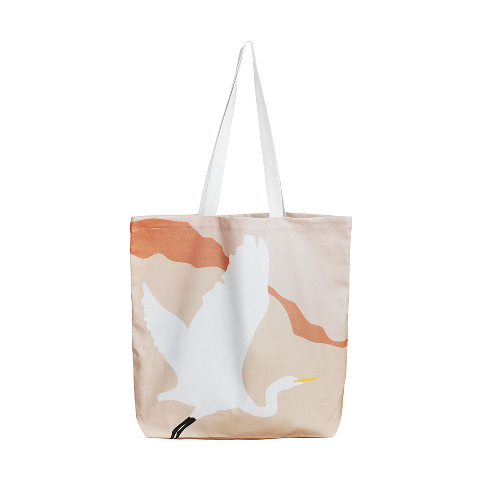 The Modern Kotuku Tote Bag is a beige cotton tote with white handles, showcasing a New Zealand Kotuku (white crane) in flight and bold orange abstract accents—perfect as a unique gift.