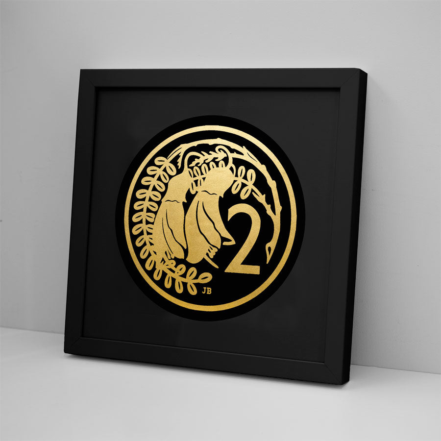 The 2 Cent Coin Foil Print features gold foil art of two birds on leafy branches beside the number 2, in a black frame that leans against a white wall for a modern Kiwiana touch.