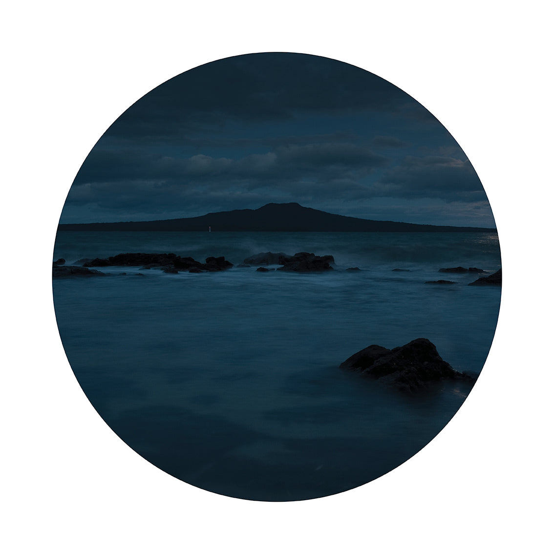 The Rangitoto Art Spot features a circular image of a tranquil blue seascape at dusk, with dark rocks and a distant island under a cloudy sky—ideal as repositionable wall art with a matte fabric finish.