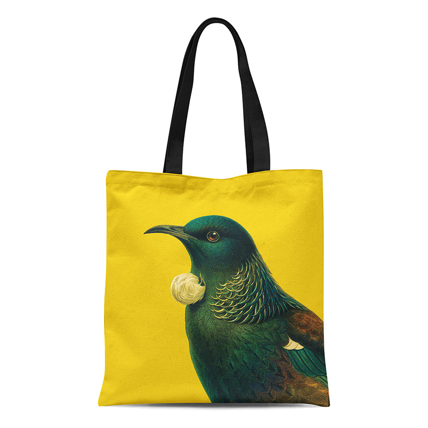 The Bright Tui Tote Bag features a vibrant tui bird on a yellow cotton background with black handles—an ideal summer accessory highlighting iridescent green and blue feathers and a striking white tuft.
