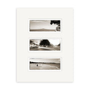 The Takapuna Triptych - RP088 features three vertically arranged black-and-white photos by Reuben Price on a white mat, showing a mountain, a New Zealand street, and a beach scene with people walking.