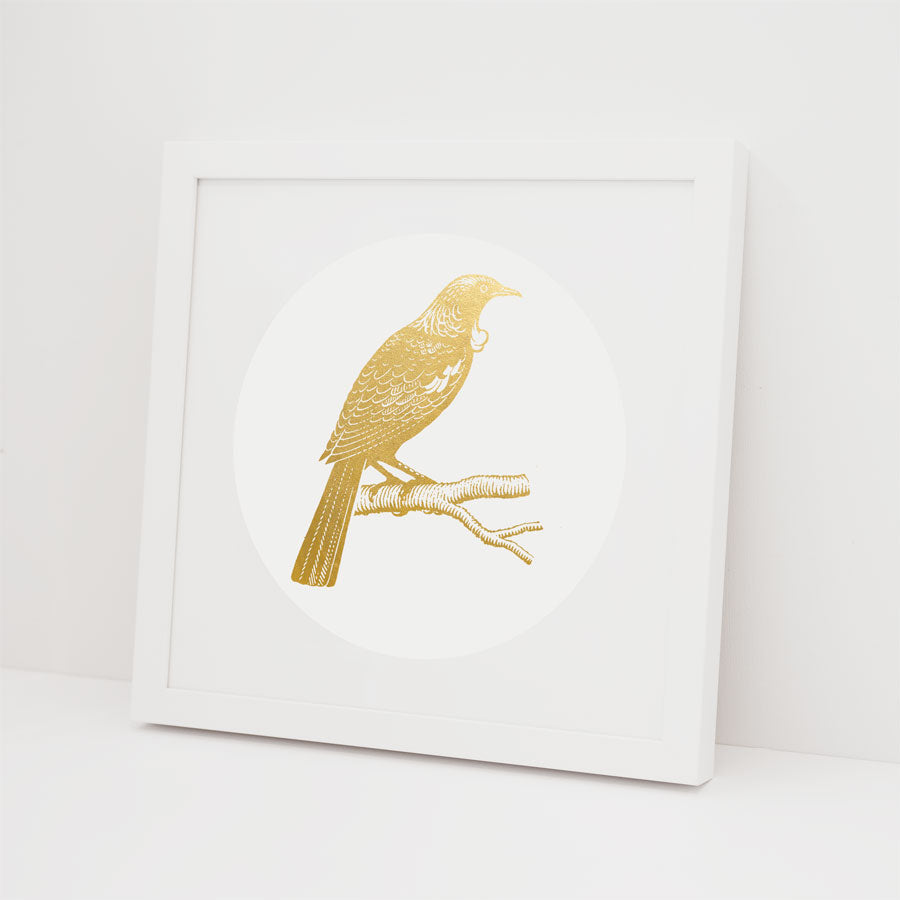The Tui Foil Print is a framed gold foil artwork of a bird perched on a branch, set on a white background. The white frame and Kiwiana-inspired design bring elegant minimalism to your space.