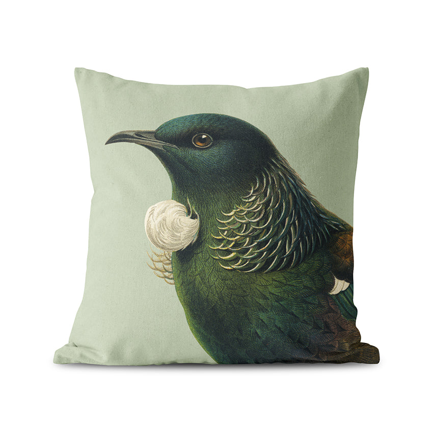 The Hushed Green Tui Cushion Cover is a square suede-feel cover featuring a detailed illustration of a New Zealand Tui bird with iridescent feathers and a white neck tuft on a light green, muted background.