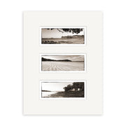The Waiheke Triptych - RP117 features three black and white New Zealand beach photographs stacked vertically on a white mat, each depicting sand, water, trees, and buildings. Printed on archival quality matte paper.