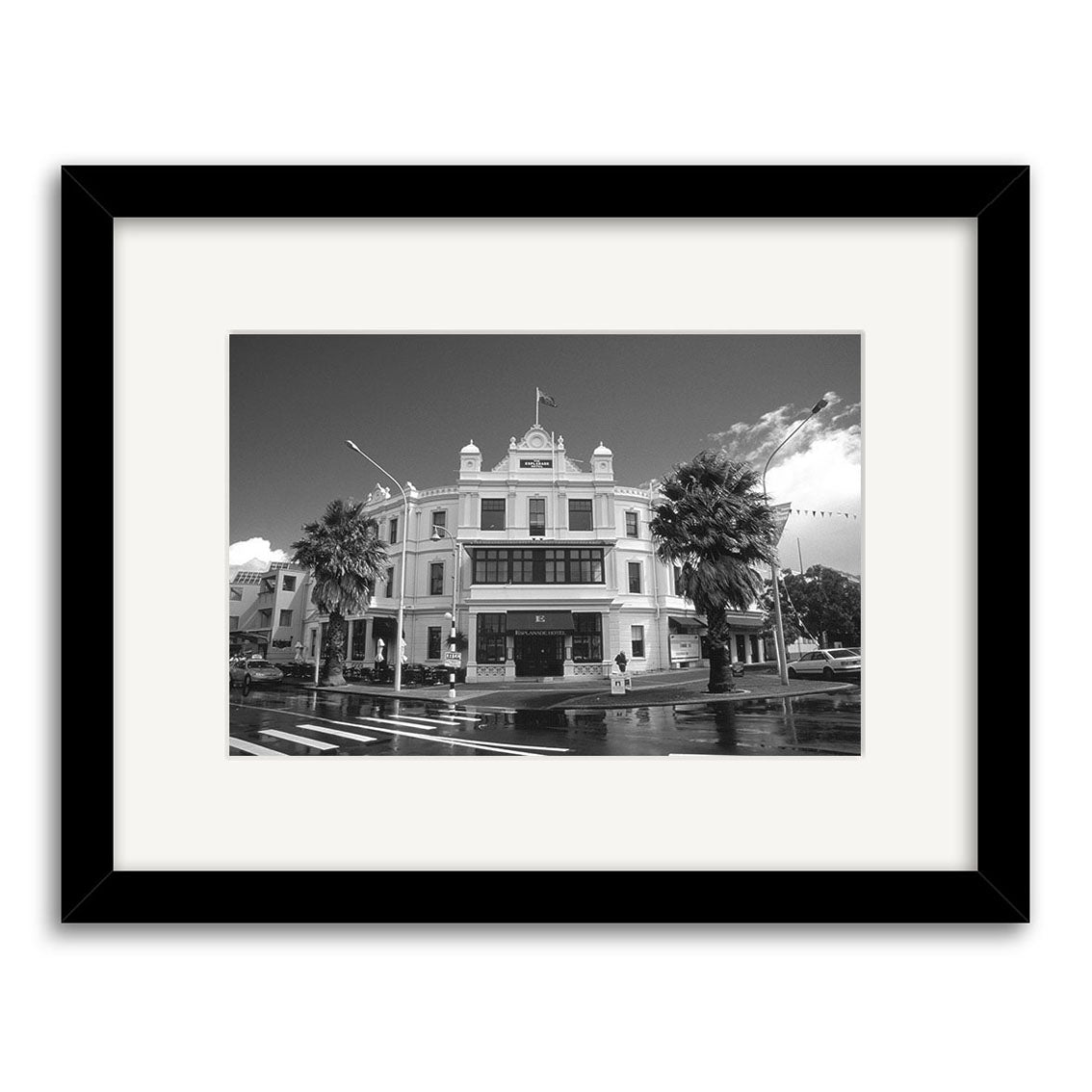 Devonport Esplanade - RP023: Black and white photo of a historic New Zealand corner building with palm trees and flag, in a black frame with white matting, printed on archival paper for lasting quality.