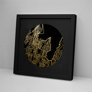 The Wellington Mapscape Foil Print is a framed art piece featuring a circular map design with gold foil streets on a black background, displayed against a white wall.