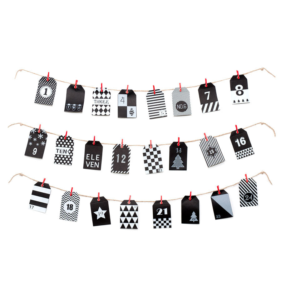 The Advent Calendar features three rows of twine with numbered black and white tags, each held by red clips. The tags display various patterns in a charming craft style, arranged from 1 to 24 for a festive countdown.