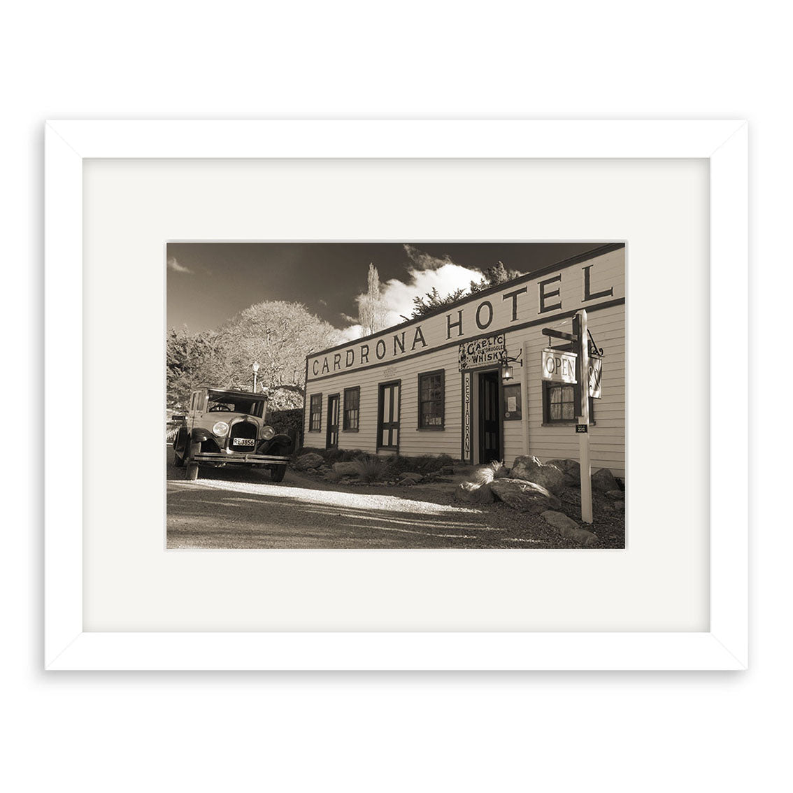 A sepia photo of the Cardrona Pub - RP071 in New Zealand, featuring its wooden facade, vintage car, and signpost. Perfect for archival matte prints, this image captures the pub’s timeless charm beneath a partly cloudy sky.